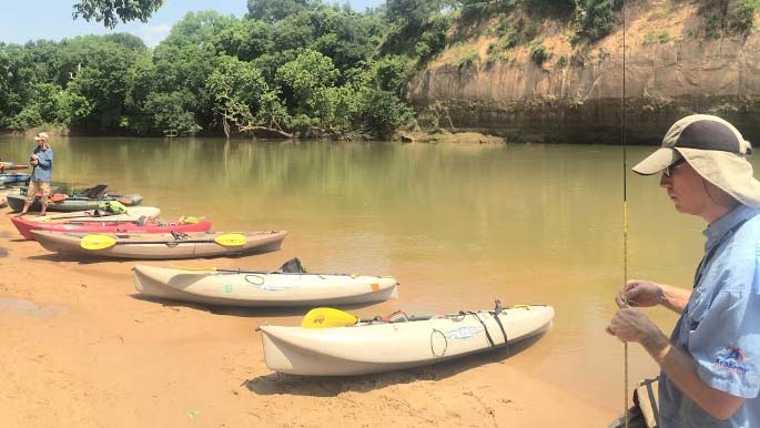 kayaks parked on red sand beach, bluff across river