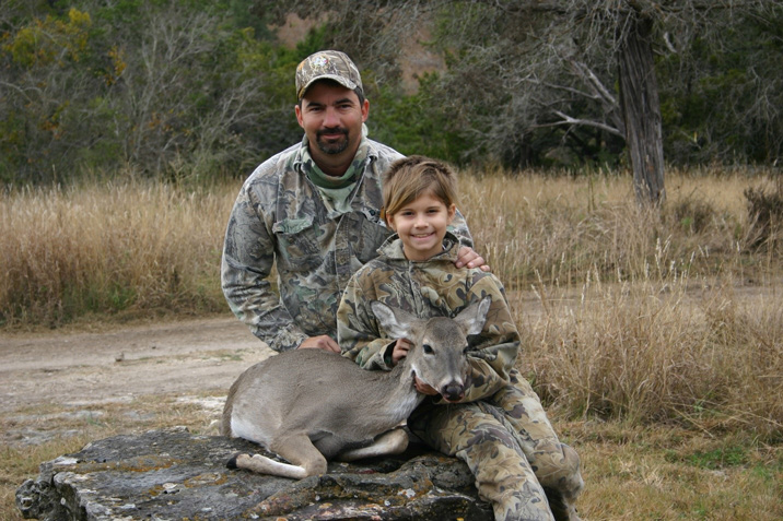 Adult hunter and child sitting on a rock with a deer