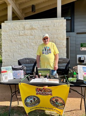 Man standing at table with Geocaching banner and materials for Geocaching program