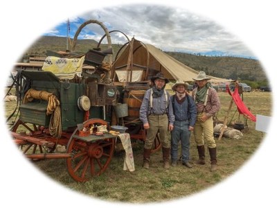 People in western wear standing in front of a chuck wagon.