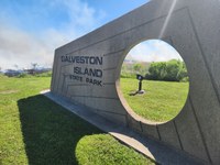 fire and smoke behind galveston island state park entrance sign