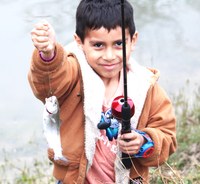 Smiling child holding a fish he caught with his fishing rod.