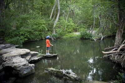 Child stands on a rock admiring the creek.