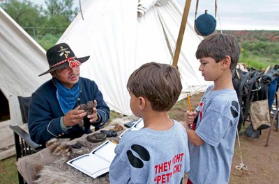 Buffalo Soldier sitting in front of table show two boys some biofacts..