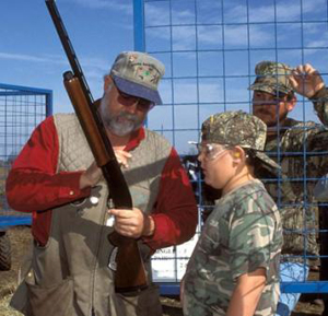 Hunting instructor reviewing gun safety procedures with a young hunter before shooting practice.