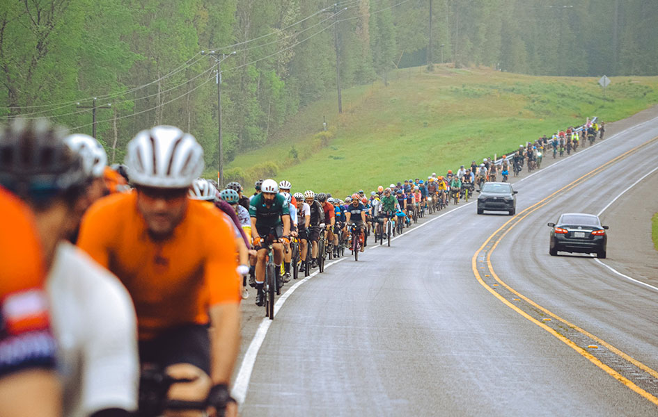 A large group of cyclists ride in the shoulder of a highway.