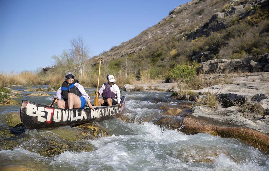 Two women in a canoe paddle a canoe as they approach a rapid.