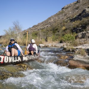 Two women in a canoe paddle a canoe as they approach a rapid