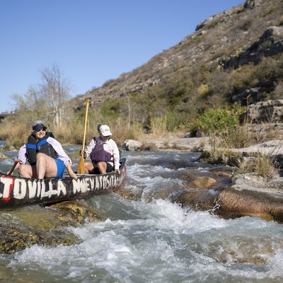 Two women in a canoe paddle a canoe as they approach a rapid