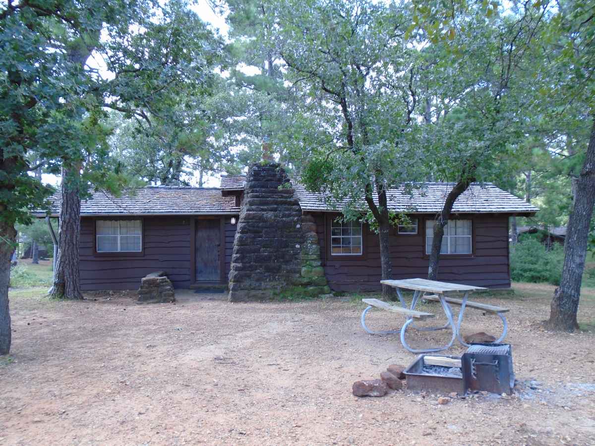 There is a picnic table and a fire ring with a grill in front of Cabin 7.