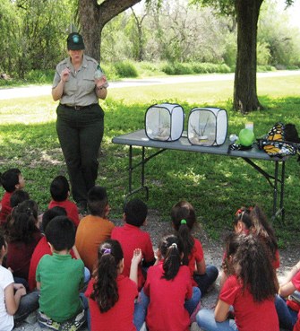 Ranger talks to group of kids seated outdoors.