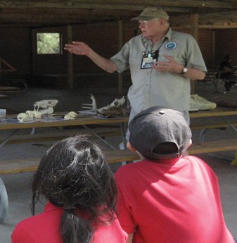 Ranger standing at a table shows items to kids.