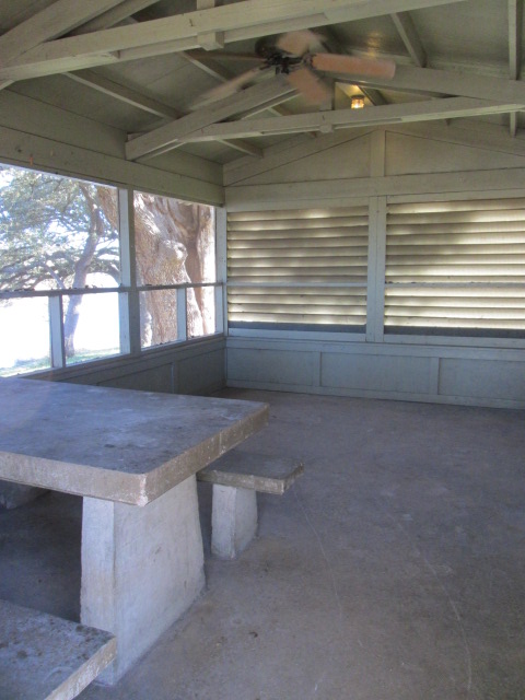Inside a screened shelter is a picnic table, light and a ceiling fan. 