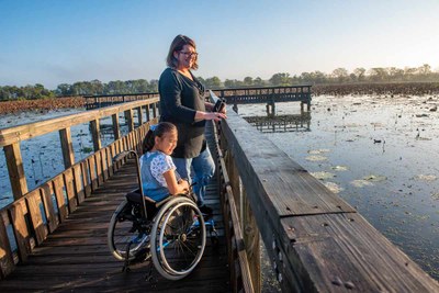 Girl using a wheelchair on a boardwalk with Mom next to her