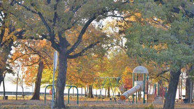 Playground equipment under trees with a lake in the background