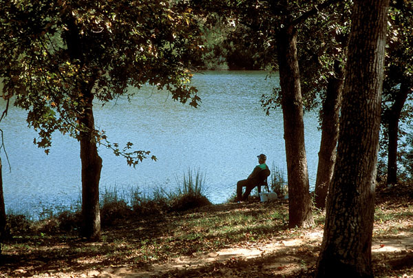 Man sitting in chair by the lake holding a fishing pole