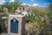 Fort Leaton Historic Site marker, surrounded by desert plants with the fort beyond.