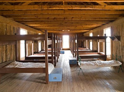 Bunk beds lined up in a large hall with storage chests at the foot of some beds.