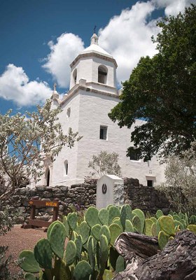 White walls of mission with bright blue sky and clouds above.