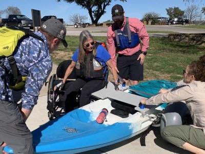 A woman uses kayak transfer to move from a wheelchair to a kayak