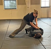 Female officer kneels on a man's back as she cuffs him.