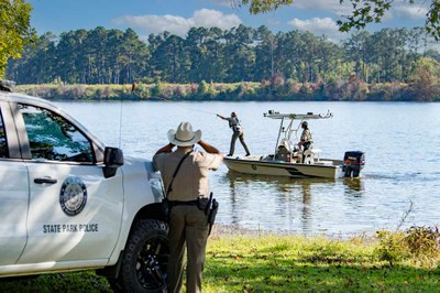 An officer on shore watches two officers in a boat, one throwing a rescue device.