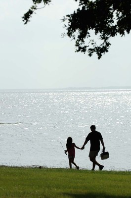 Silhouette of father and daughter by lake carrying fishing gear