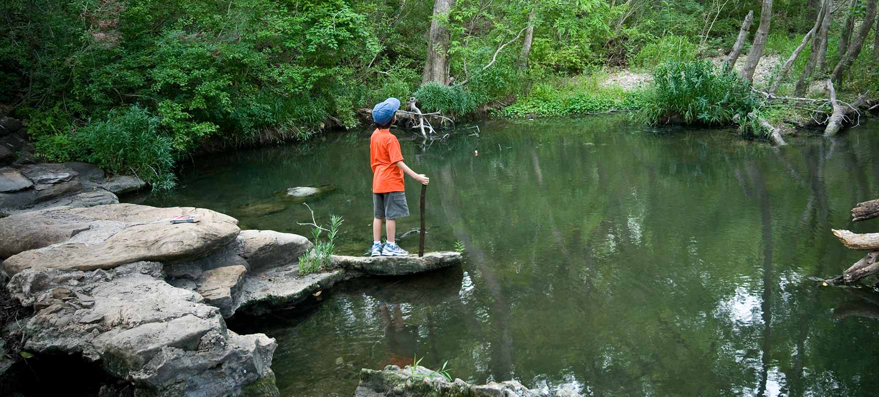 Kid With Hiking Stick by Creek