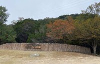 View of Lost Maples sign and fence with vari-colored trees behind