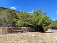 Lost Maples park sign and fence with green trees behind.