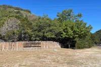 Lost Maples park sign and fence with green trees behind.