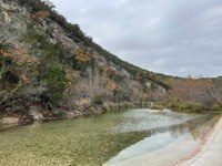 Hillside with river in the foreground. A few trees still have colorful leaves.