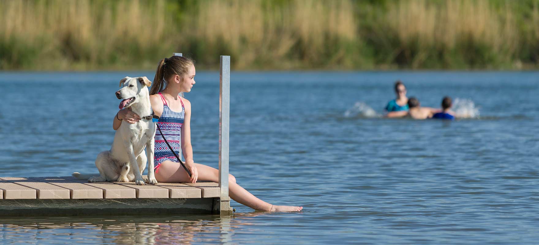 Girl and dog sitting on pier.