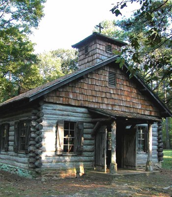 Mission building with door open and wooden cross on top of building