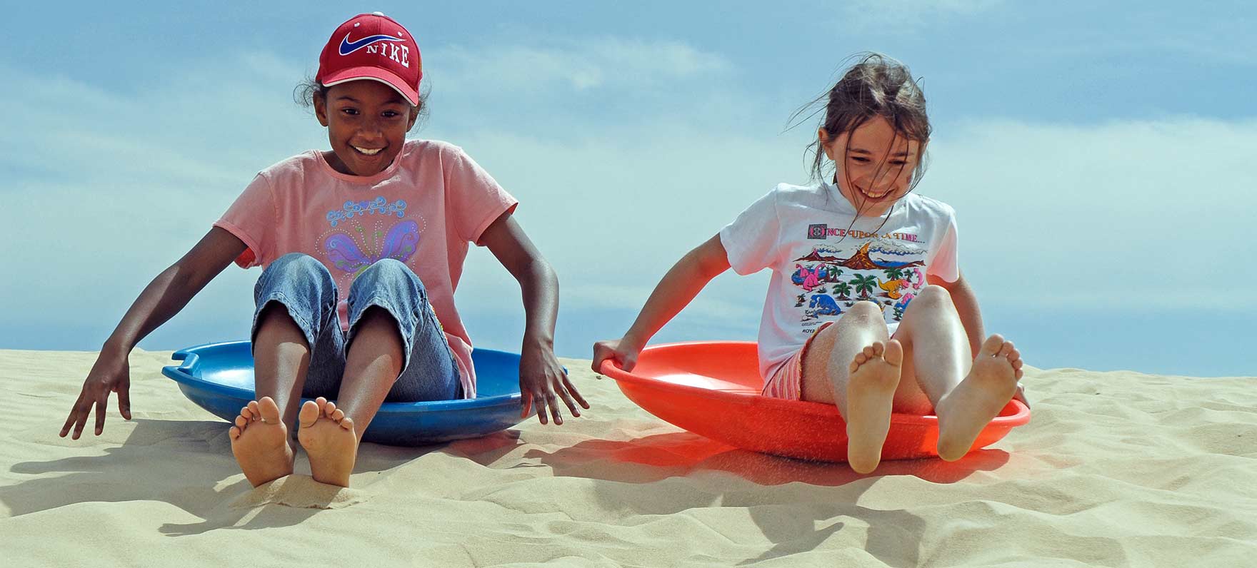 girls laughing and surfing down sand dune