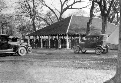 Black & white photo of pavillion with old cars parked in front.