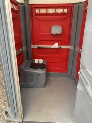 Inside of the ADA portable toilet - there is a handrail and toilet with seat, and space for a wheelchair.