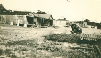 Sepia toned photo of some primitive buildings and pipes laid out on the ground.