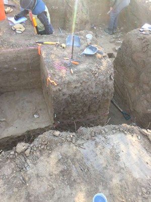 Squared out pit in the ground, with tools scattered about and people working on the edges