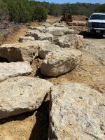 Large boulders lined up with park vehicle and bobcat in the background.