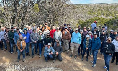 Large group of people wearing work clothes pose on the edge of an overlook of the countryside.