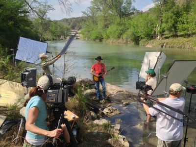 Group of people filming a guitar player on a ledge overlooking a lake.
