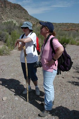 Two women pausing on a hike, wearing hats and hiking boots.