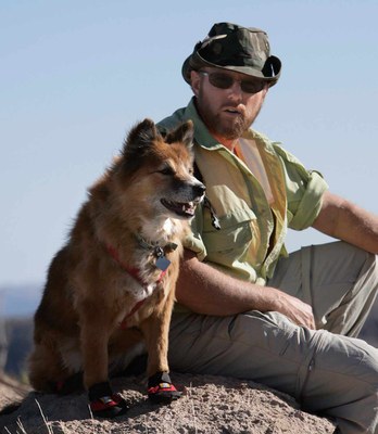 Hiker and his dog sitting on a rock. Dog is wearing booties