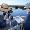 Person taking a photo while another looks in a bird book
