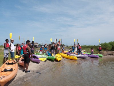 Group of people in life jackets standing next to kayaks on lake shore