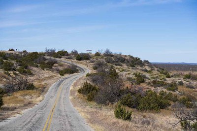 A road winds up a hill at San Angelo State Park under a bright blue sky