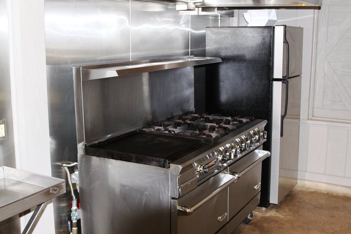 There is a commercial stove/oven, vent hood with fire suppression system, refrigerator, freezer, and microwave.